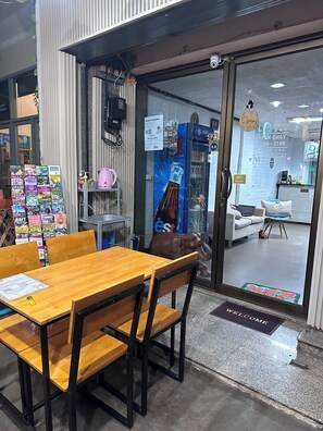 A cafe with a wooden table and chairs, a glass door entrance, and a sign indicating room availability. - J cafe & hostel (Chiang Mai)