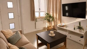 En stue med sofa, sofabord, fjernsyn og et vindue med gardiner.