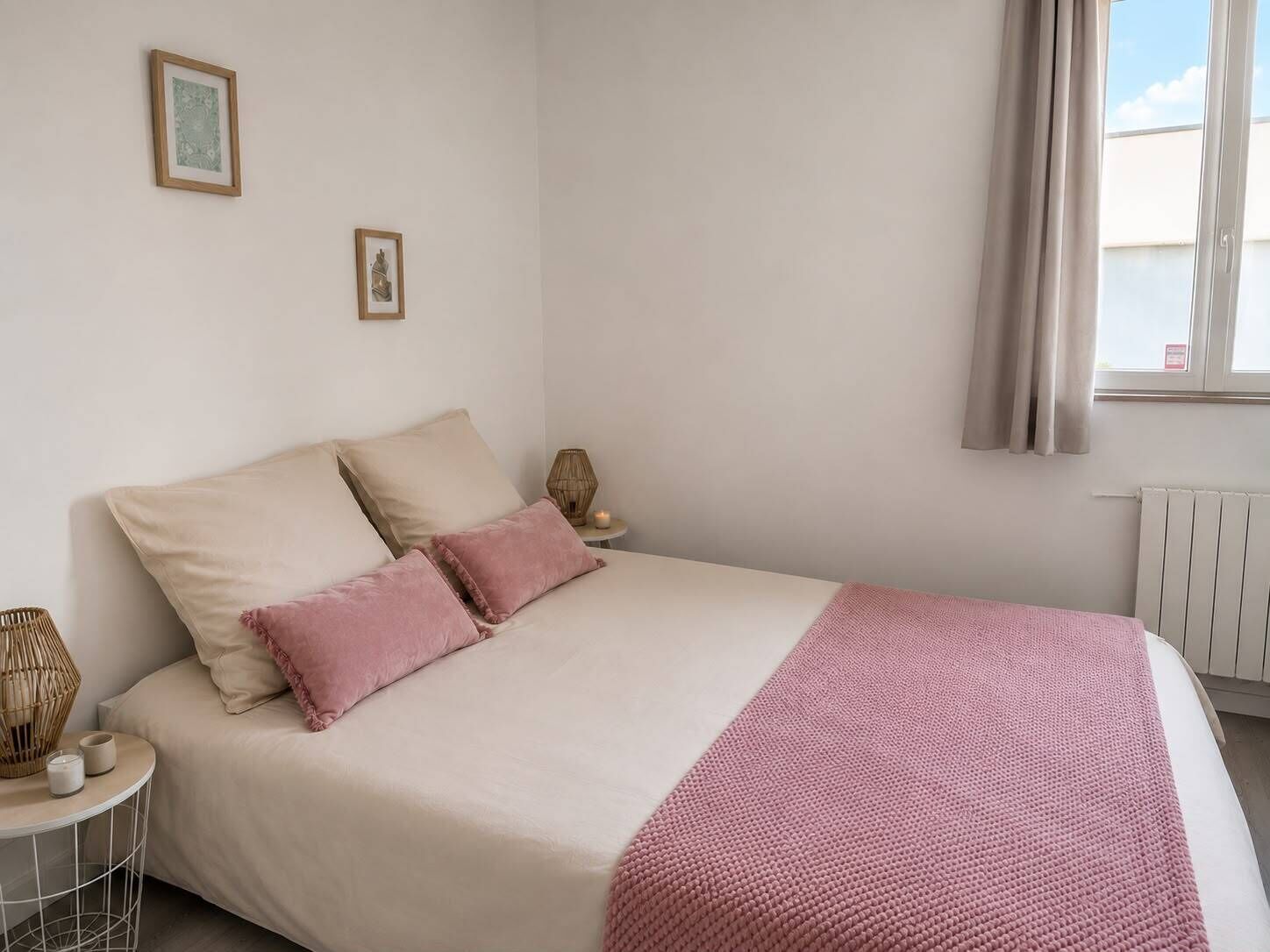 Un dormitorio con cama, almohadas, una mesita de noche con una vela y una ventana con cortinas.