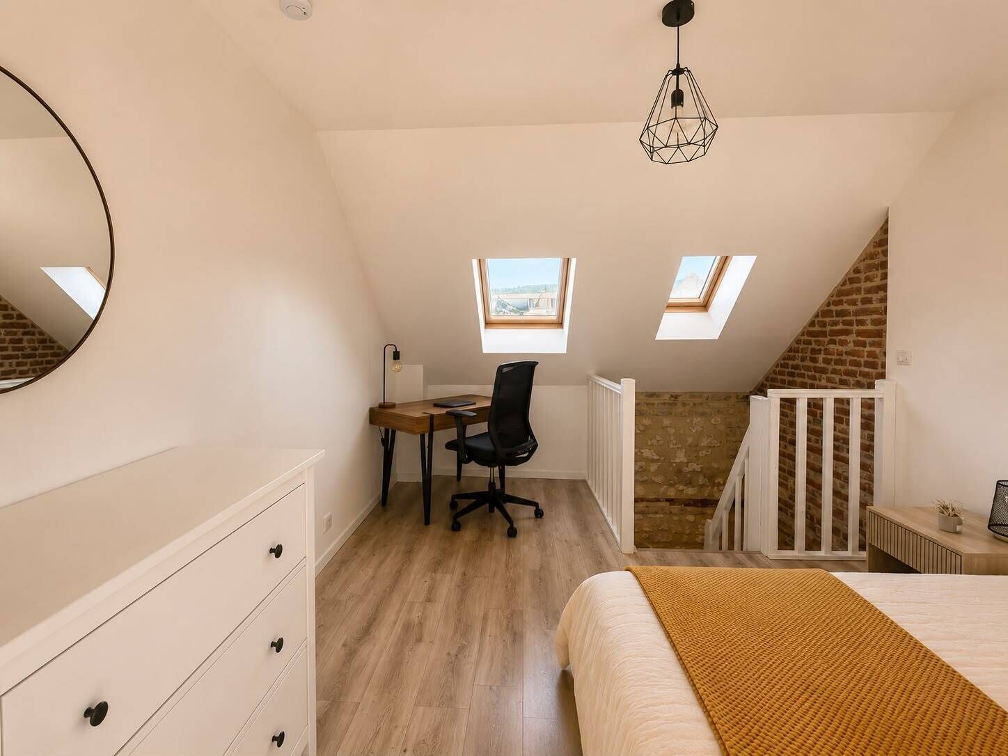 Ein Schlafzimmer mit Bett, Schreibtisch, Stuhl, Kommode und Dachfenstern.