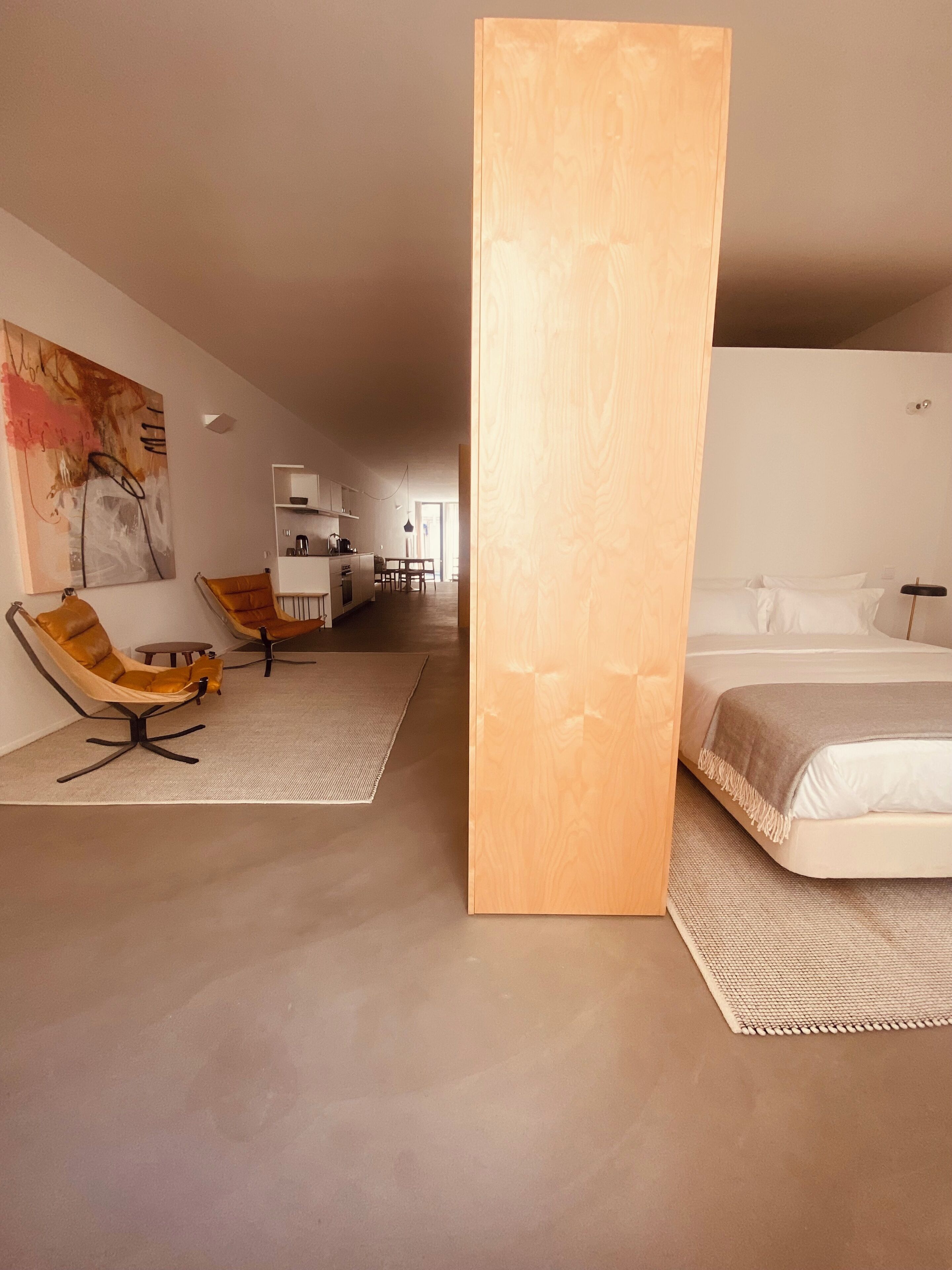 A modern hotel room with a large bed, a sofa, and a dining area in the background.