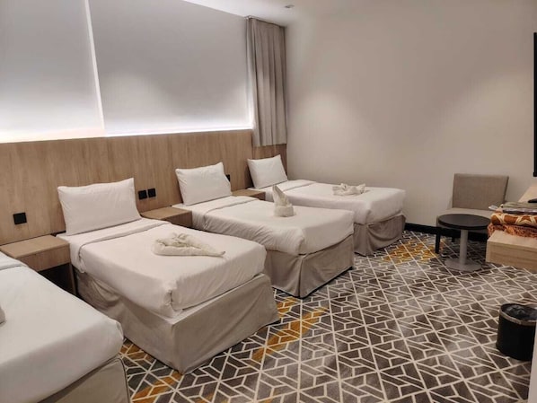 Habitación de hotel con tres camas, una mesita, una silla y piso con diseño.