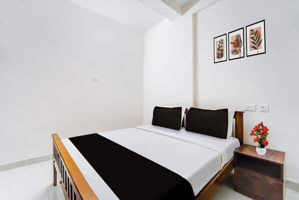 Un dormitorio con una cama, una mesita de noche, un florero con flores y tres cuadros en la pared.