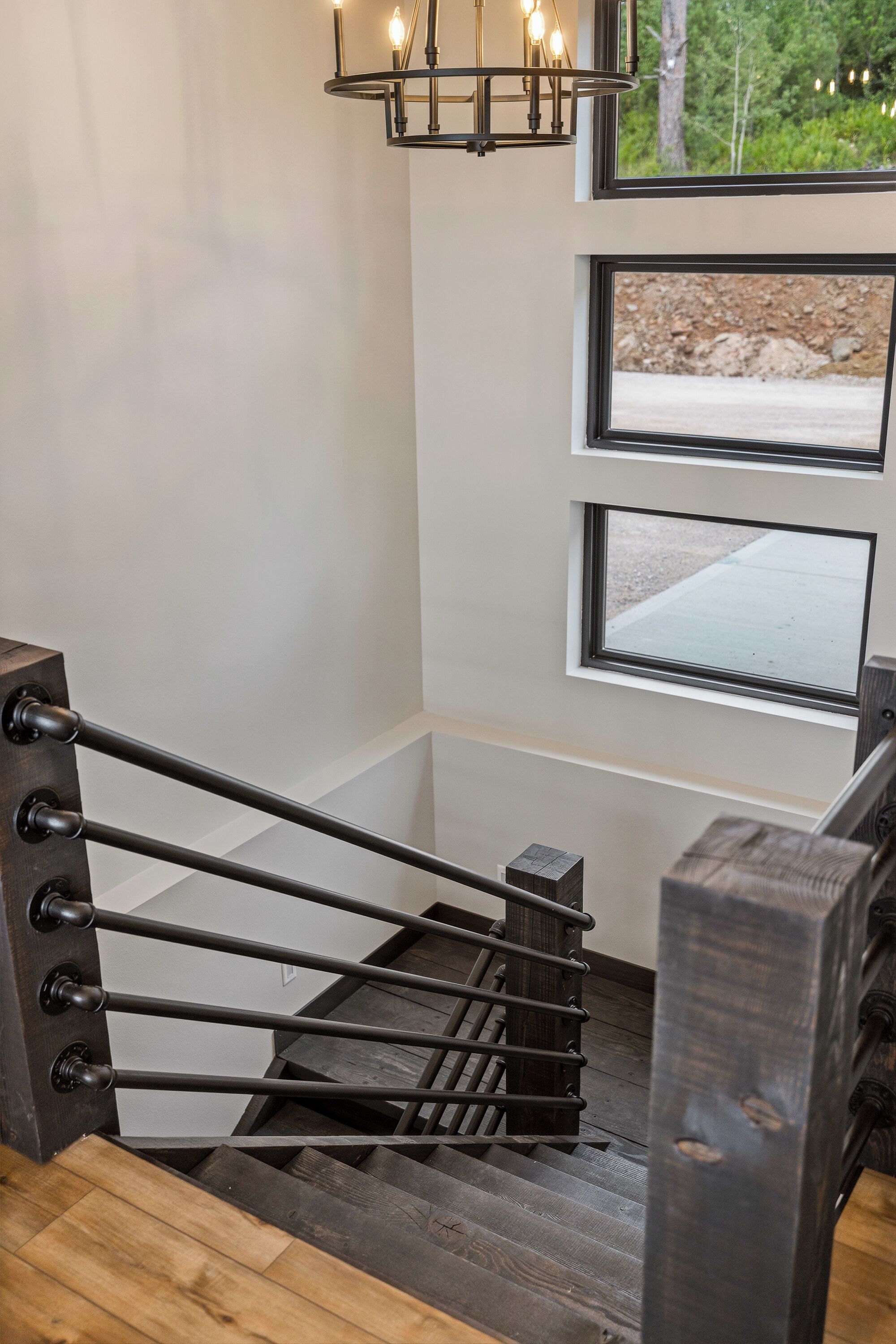 A staircase with a metal handrail and wooden steps, leading to a landing with a view of a landscaped area.