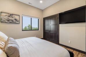 A bedroom with a bed, a window, a door, and a wall-mounted TV. - New Hilltop Escape, Sweeping Black Hills Views w/ Hot Tub, Large Driveway (Lead)