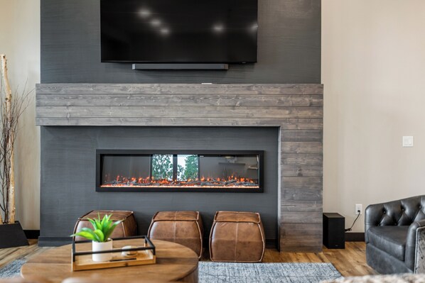 Un salon moderne doté d’un téléviseur à écran plat fixé au-dessus d’une cheminée, de sièges en cuir et d’un plancher en bois.