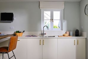 A kitchen with a window, a sink, a chair, and a television. - Finest Retreats | Wobbly Cod (Charlestown)