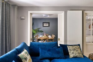 Ein Wohnzimmer mit einem blauen Sofa, einem Esstisch mit Stühlen und einer Tür zu einem anderen Raum.