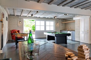 A room with a pool table, a red chair, a bottle of beer, and a foosball table.