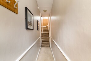 A narrow hallway with a carpeted staircase leading to a landing. - Brick & Beam on Tabard (London)