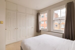 A bedroom with a large bed, a wardrobe, and a window with a view of buildings. - Brick & Beam on Tabard (London)