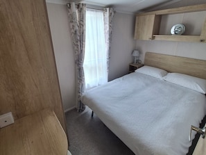 Un dormitorio con cama, mesita de noche, lámpara, estante de madera y ventana con cortinas.