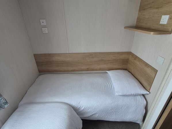 Habitación pequeña con una cama individual, cabecera de madera y un estante.