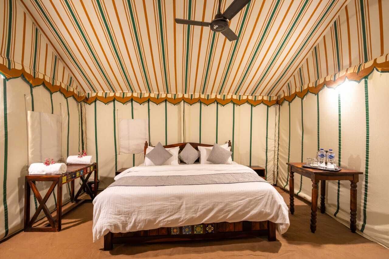 Una habitación con una cama, un ventilador de techo, una mesita de noche con una botella de agua y una pared con rayas verticales.