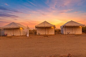 Três tendas com vista para o deserto e um pôr do sol ao fundo.