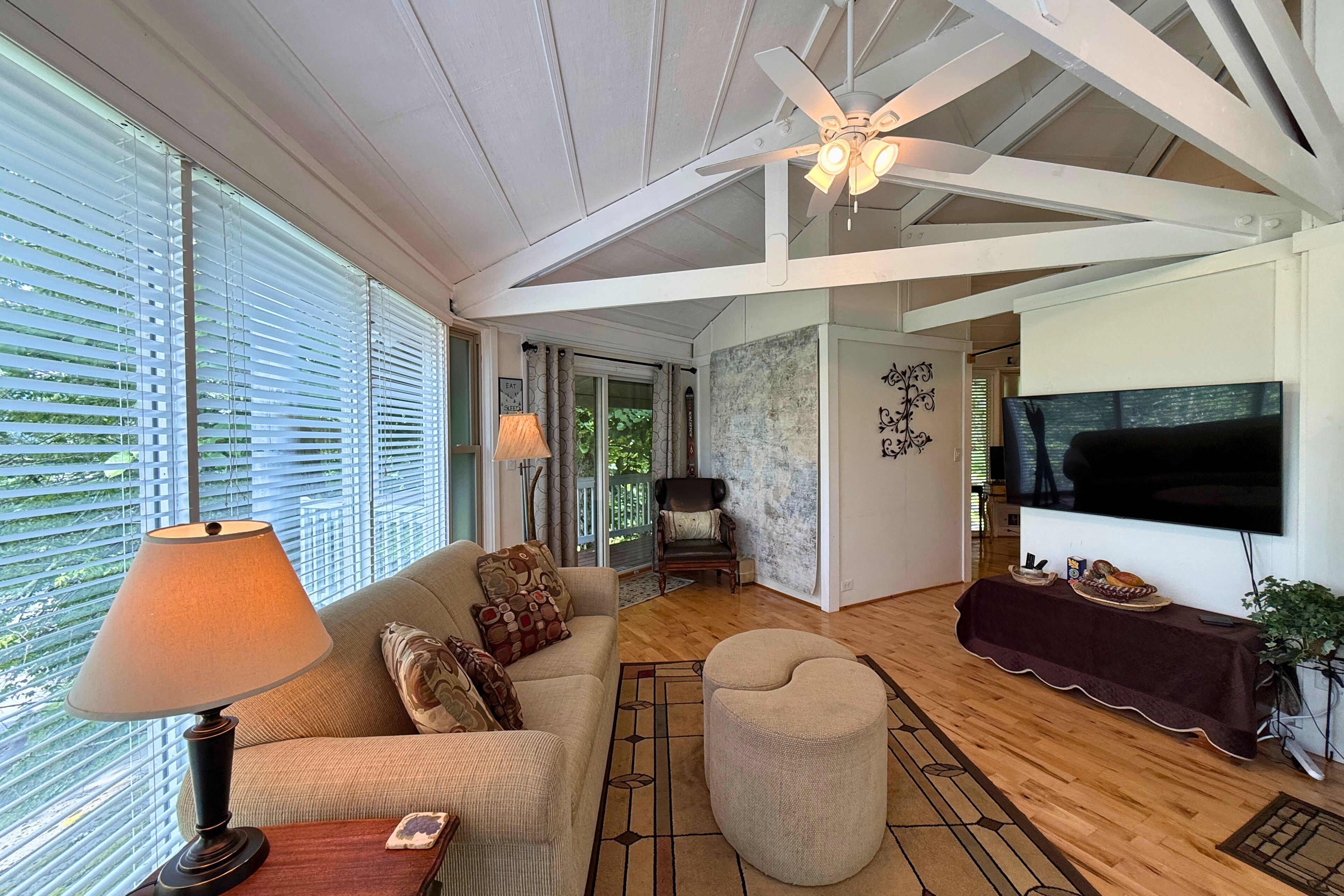 A spacious living room with a ceiling fan, a television, and a large window with blinds.