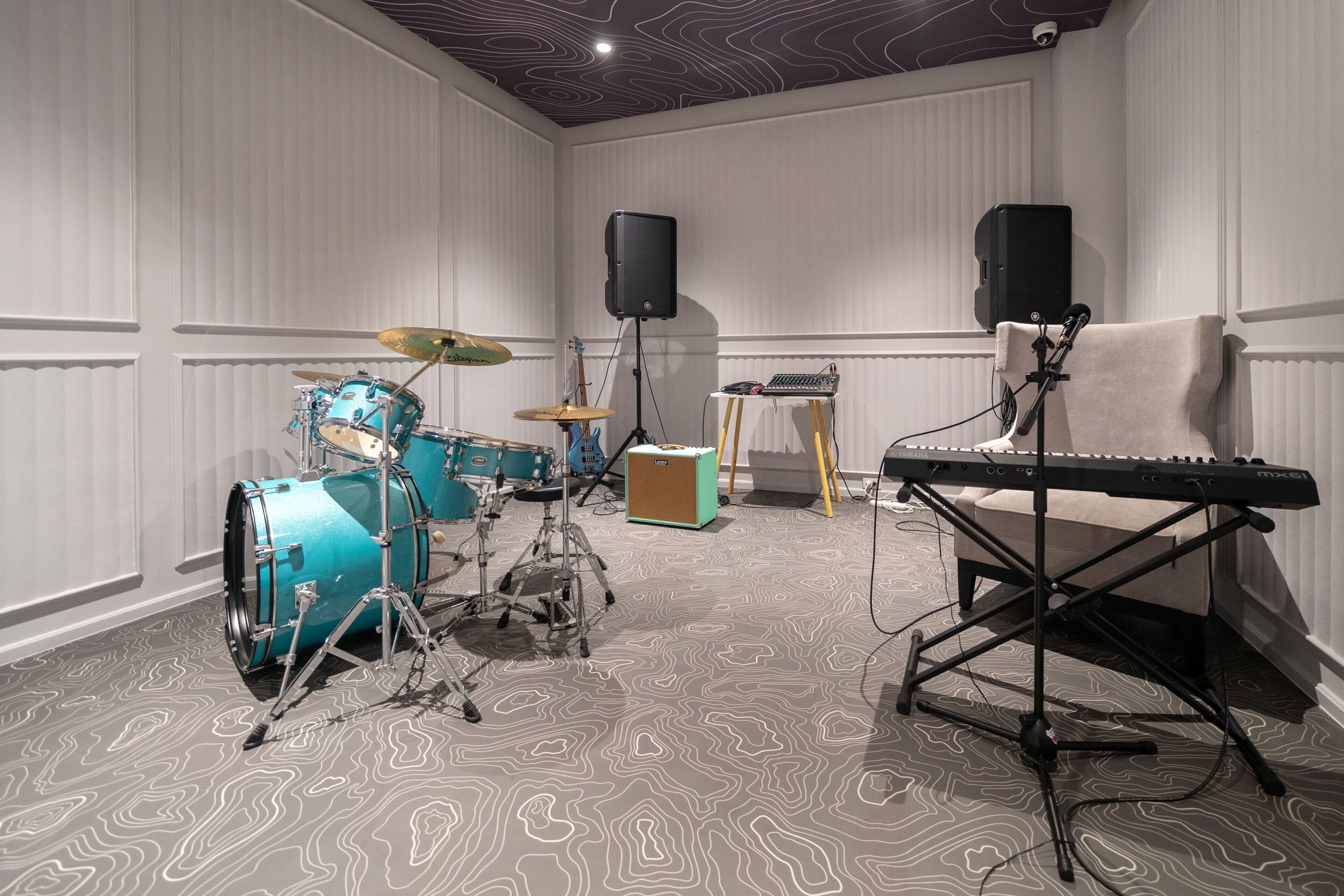 Una habitación con batería, teclado y altavoces, que sugiere un espacio para ensayar o actuar música.