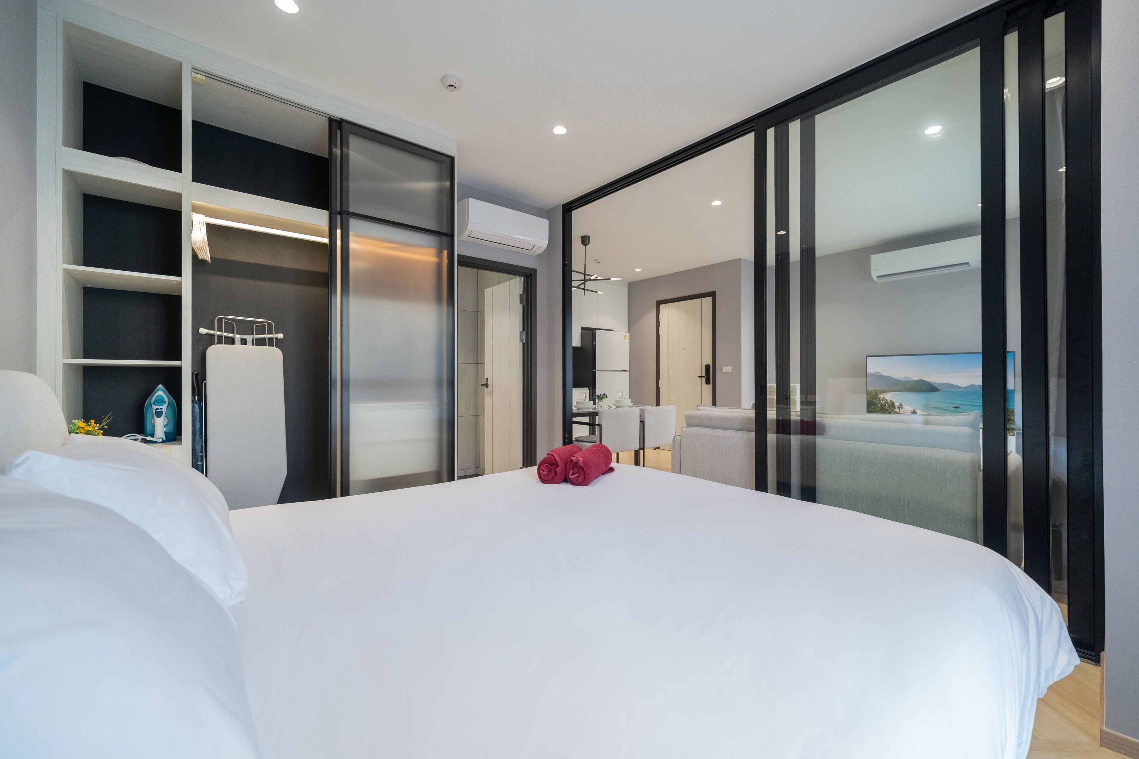 Habitación de hotel moderna con una cama grande, vestidor, kitchenette y vistas al mar.