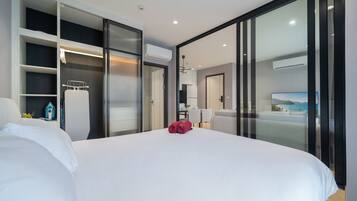 Habitación de hotel moderna con una cama grande, vestidor, kitchenette y vistas al mar.