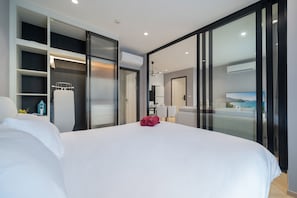 Habitación de hotel moderna con una cama grande, vestidor, kitchenette y vistas al mar.