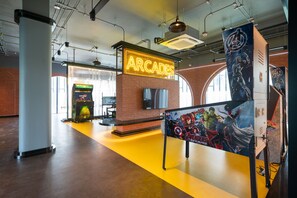 Un área de juegos modernos con letreros de neón, máquinas de juego y un cartel grande de personajes de Avengers.
