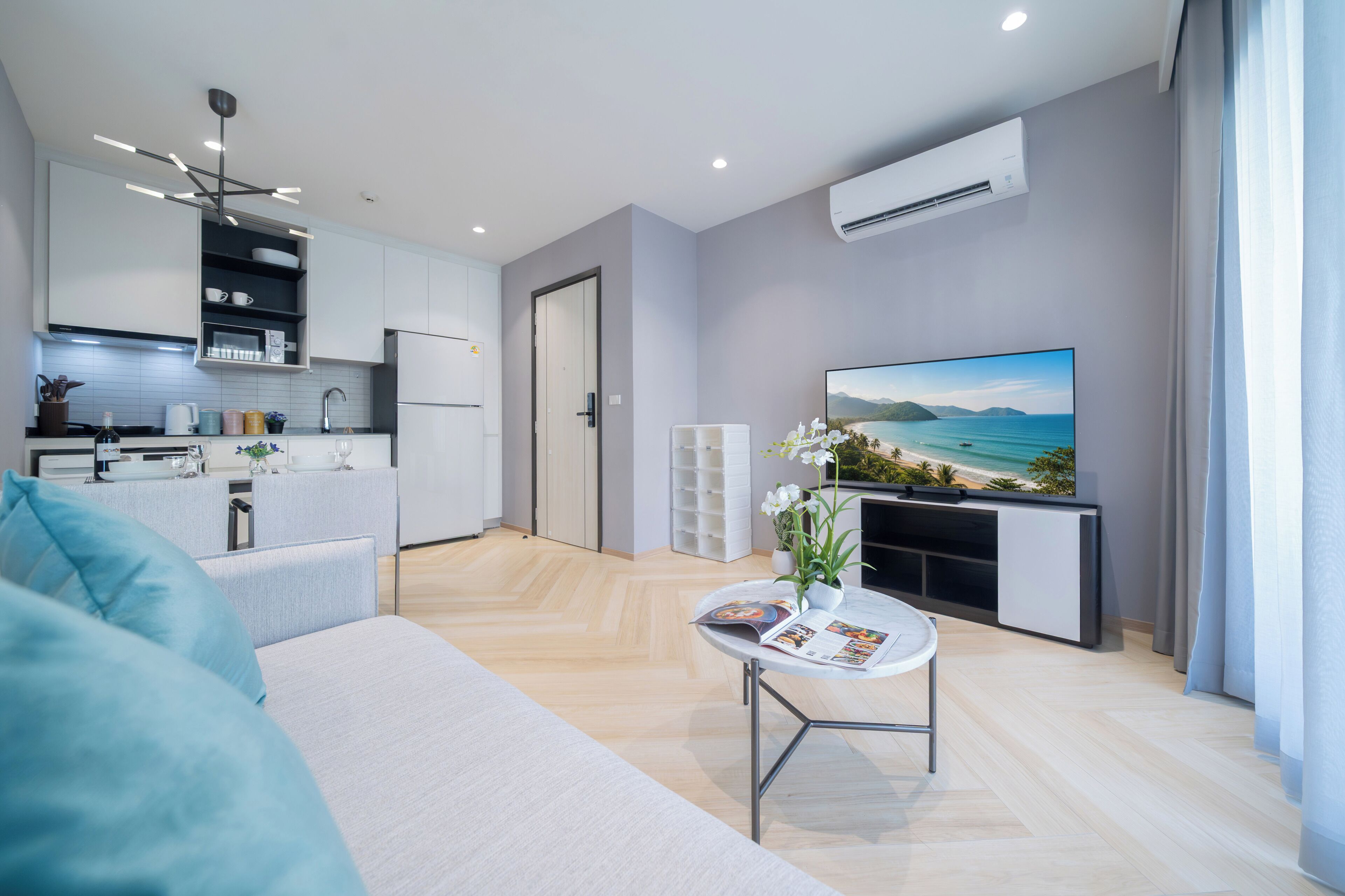 Una sala de estar moderna con un sofá, una mesa de centro con revistas, un televisor y una cocina al fondo.
