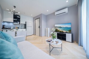 Una sala de estar moderna con un sofá, una mesa de centro con revistas, un televisor y una cocina al fondo.
