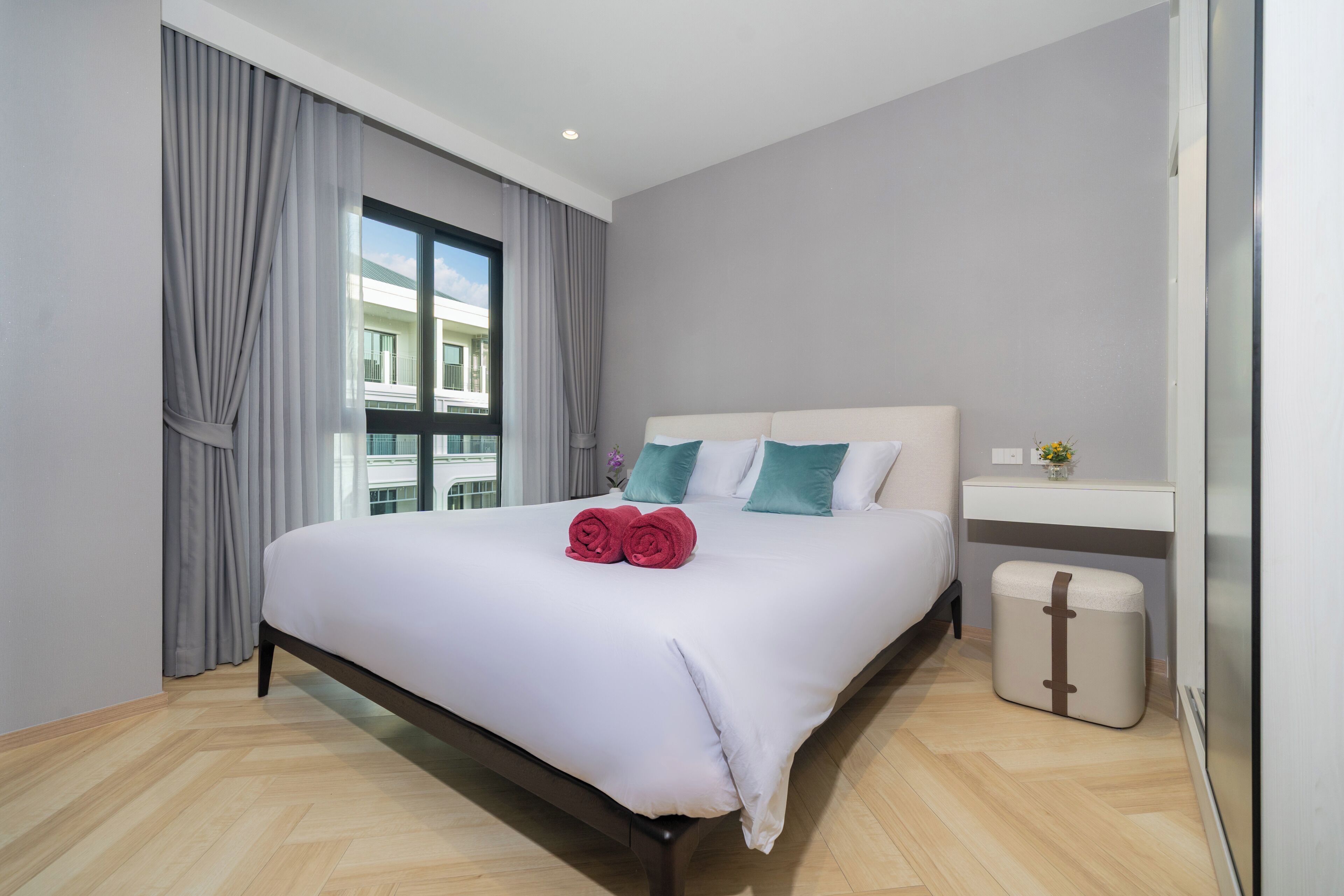 Habitación de hotel con una cama grande, una mesita de noche, un cesto de basura pequeño y una ventana con cortinas.