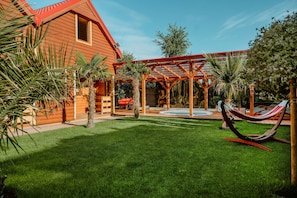 A wooden house with a red roof, a covered patio area, and a hammock. - Comfortable Houses With a SPA Zone (Kamien Pomorski)