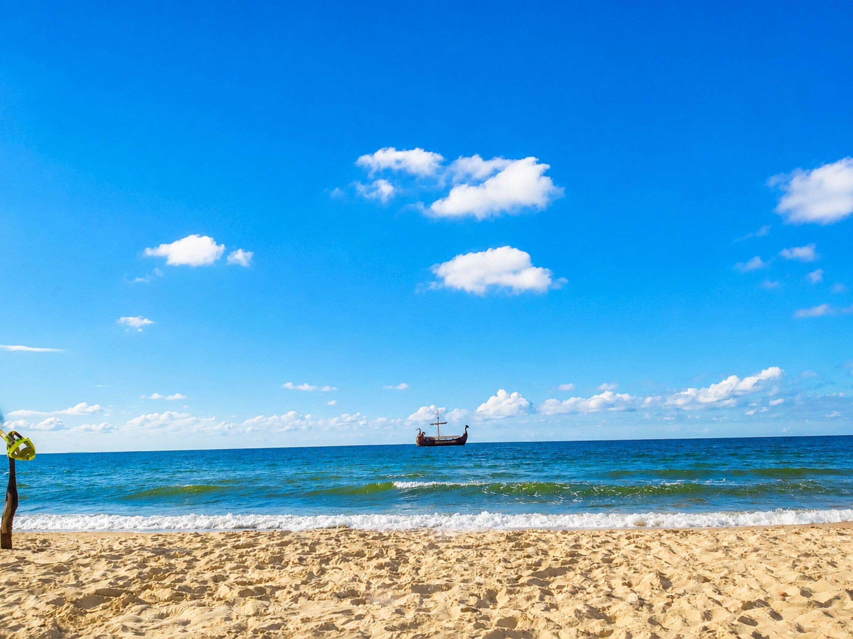 A beach with a boat in the distance, clear skies, and calm sea.