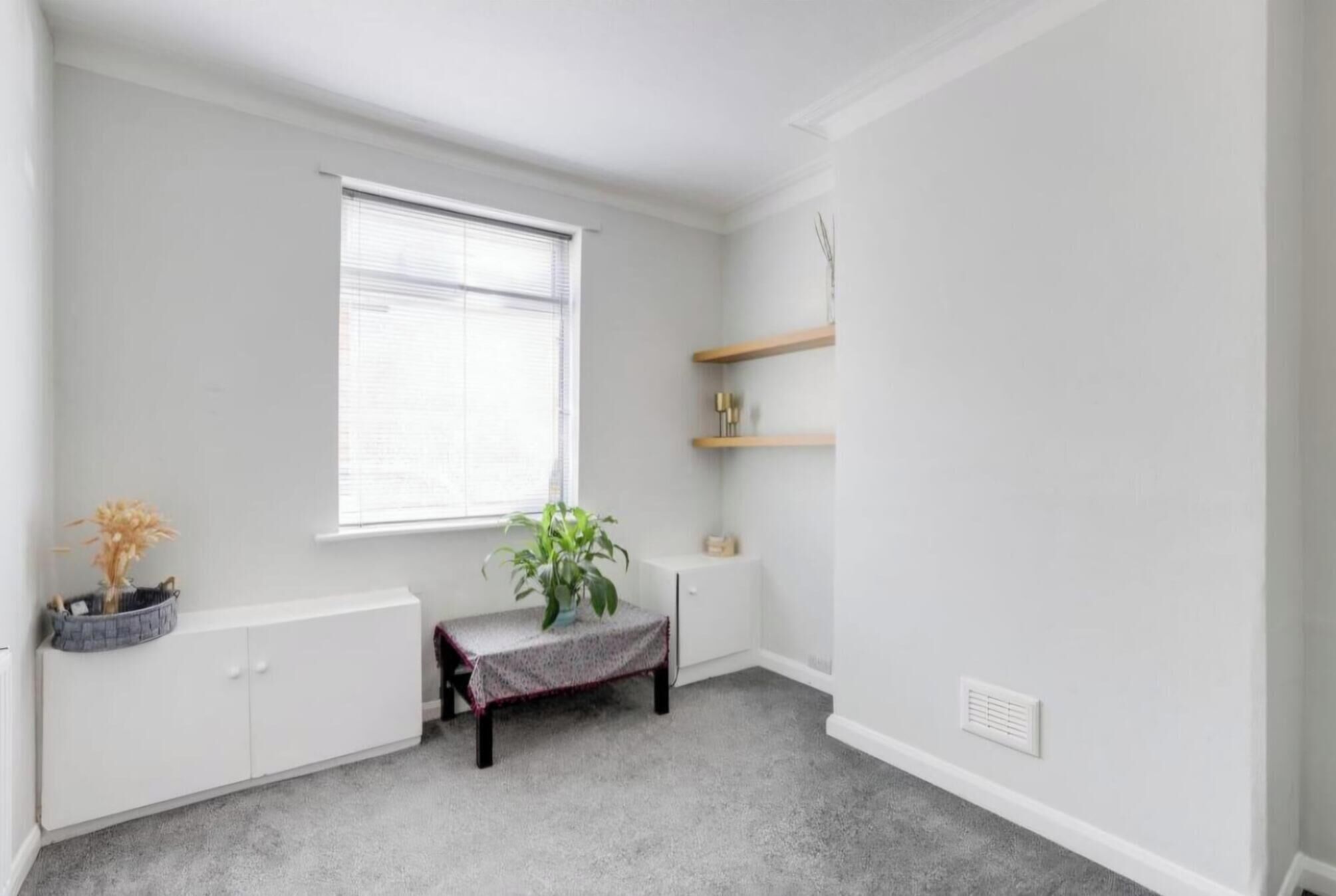 A room with a radiator, a window with blinds, a bench, a potted plant, and a white cabinet.