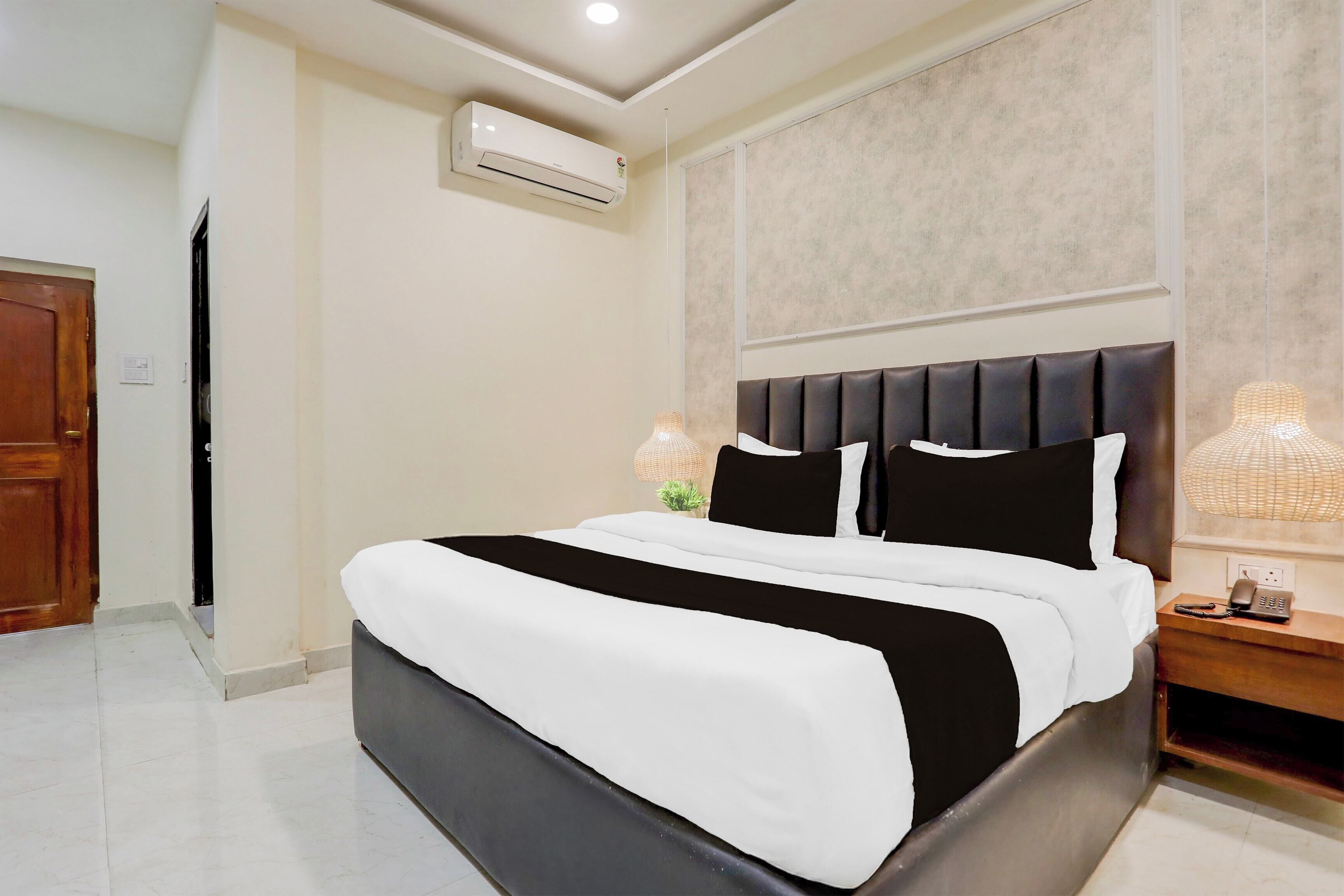 Una habitación de hotel con cama, mesita de noche, lámpara y aire acondicionado.