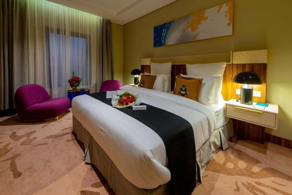 Habitació d'hotel amb un llit gran, una taula de treball, una cadira i una finestra amb cortines.