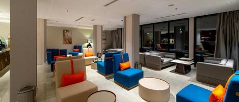 A modern hotel lobby with multiple seating areas, including sofas and armchairs, a coffee table, and a trash bin.