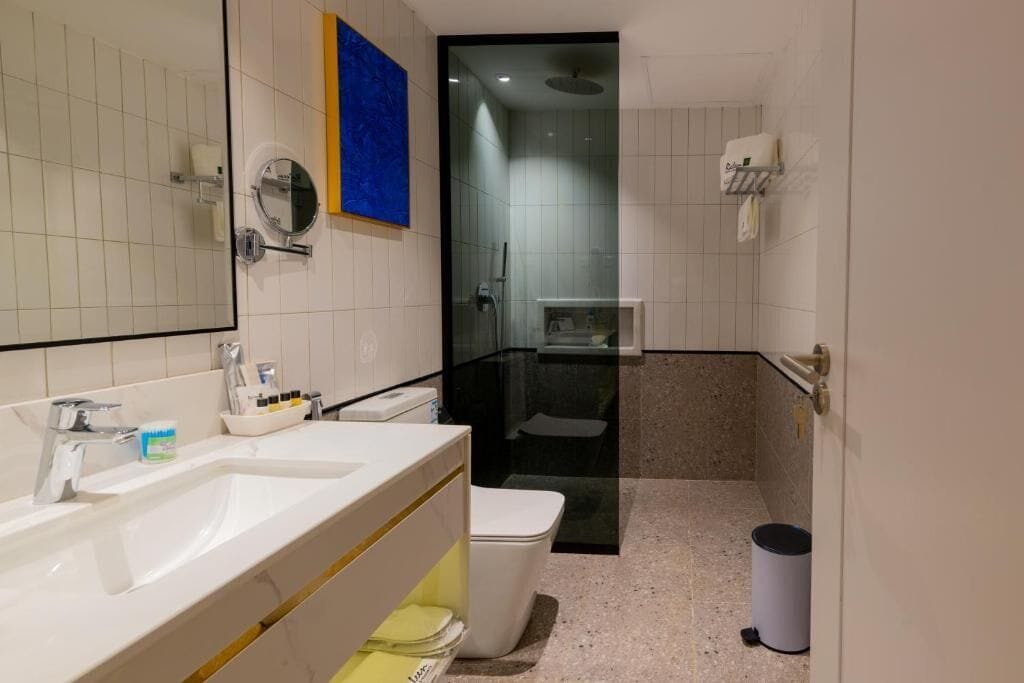 A modern bathroom with a double sink, toilet, and glass-enclosed shower.