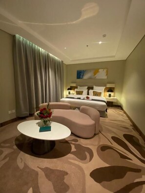 A hotel room with a bed, a sofa, a round coffee table, and a large window with curtains. - Raleen Hotel (Al Wajh)