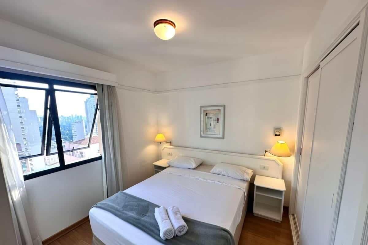 Una camera d'albergo con un letto, lampade sui comodini, una finestra con tende e vista sulla città.