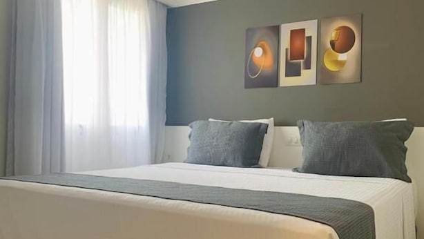 Ett hotellrum med en stor säng, ett fönster med gardiner och två konstverk som hänger på väggen.