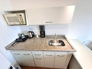 Una cucina compatta con microonde, bollitore e un piccolo lavandino.
