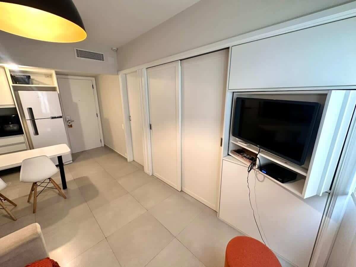 Un ambiente compatto con angolo cottura, zona pranzo con tavolo e sedie e televisore a parete.