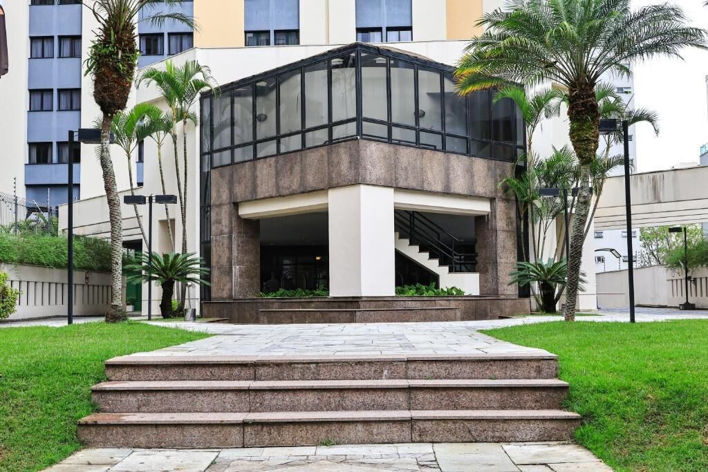 Un edificio moderno con facciata in vetro, un ingresso centrale con gradini e palme sullo sfondo.