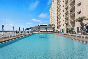 A swimming pool with a covered area, lounge chairs, and a high-rise building in the background. - NEW! Wet Bar, Beachfront, Fully Renovated, 3 Pools, Hot Tub, Gym (Panama City Beach)