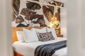 A bed with white bedding and multiple pillows, a wooden headboard, and a wall with a floral pattern. - NEW! Wet Bar, Beachfront, Fully Renovated, 3 Pools, Hot Tub, Gym (Panama City Beach)