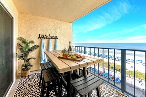 A balcony with a table set for dining, a potted plant, and a view of the beach. - NEW! Wet Bar, Beachfront, Fully Renovated, 3 Pools, Hot Tub, Gym (Panama City Beach)