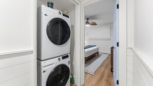 Een wasserette met twee gestapelde wasmachines en een bed in de aangrenzende kamer.