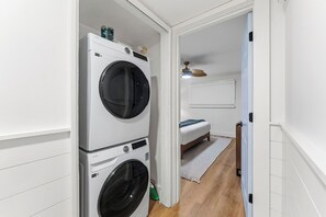 A laundry room with two stacked washing machines and a bed in the adjacent room. - NEW! Wet Bar, Beachfront, Fully Renovated, 3 Pools, Hot Tub, Gym (Panama City Beach)