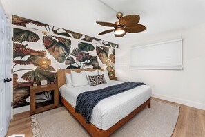 A bedroom with a bed, a nightstand, a ceiling fan, a wall with a leaf pattern, and a window with blinds. - NEW! Wet Bar, Beachfront, Fully Renovated, 3 Pools, Hot Tub, Gym (Panama City Beach)