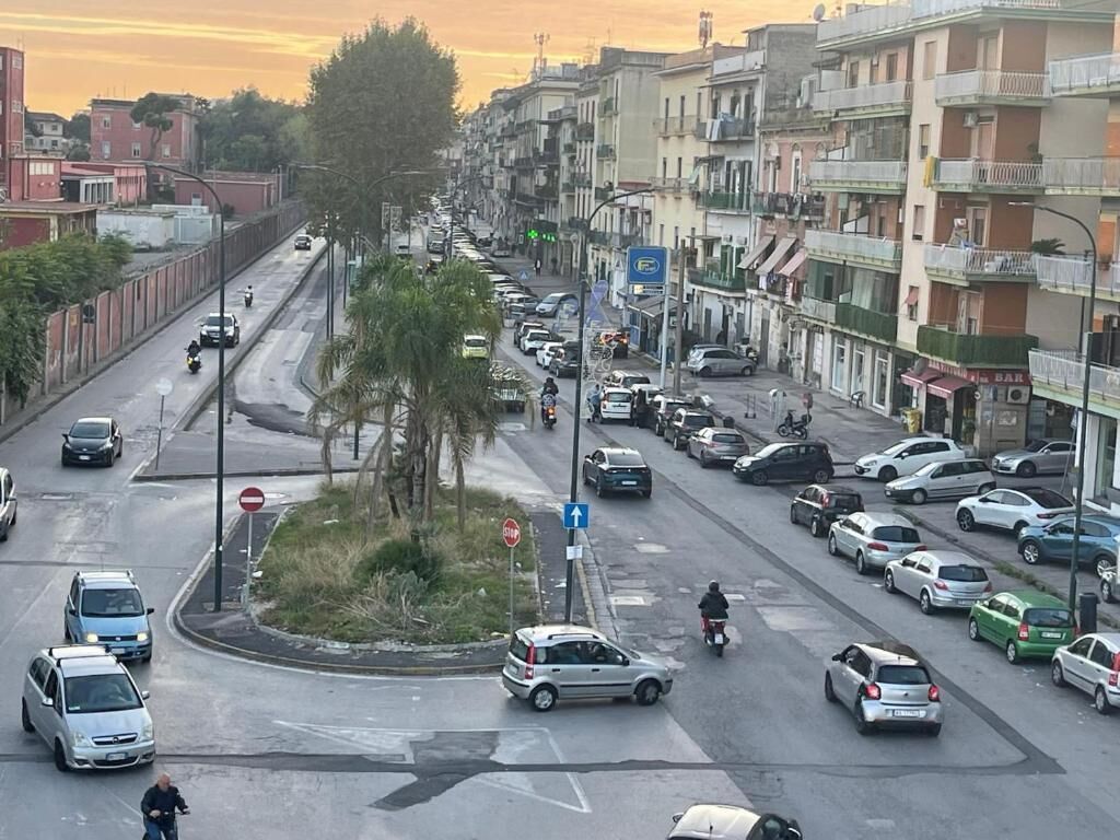 Una concurrida calle urbana con múltiples carriles de tráfico, incluyendo automóviles y motocicletas. Hay edificios a ambos lados de la calle, con algunas tiendas y viviendas.