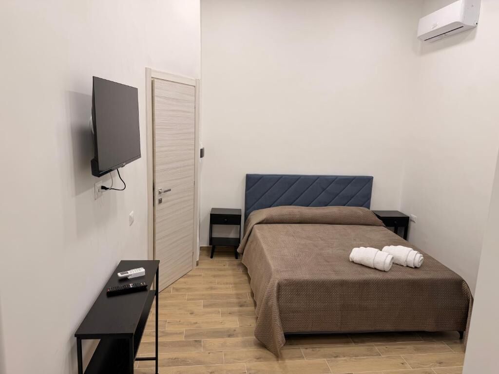 Un dormitorio con cama, televisor montado en la pared, mesita de noche y una pequeña consola.