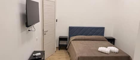 Un dormitorio con cama, televisor montado en la pared, mesita de noche y una pequeña consola.